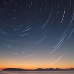 A stunning long exposure of star trails over the ocean horizon at twilight.