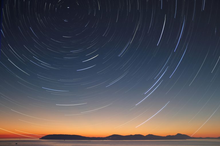 A stunning long exposure of star trails over the ocean horizon at twilight.